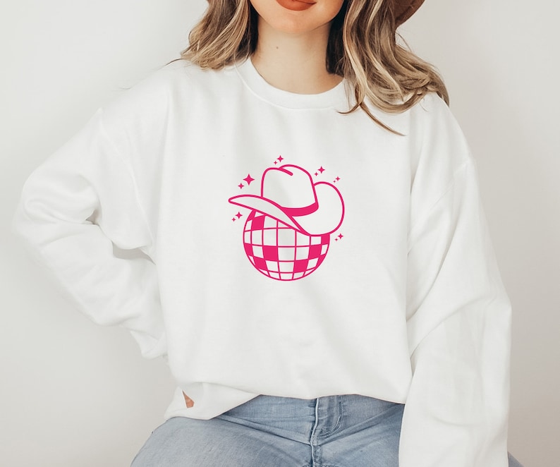 Pu&ograve; includere: Felpa bianca con una grafica rosa di una palla da discoteca che indossa un cappello da cowboy.