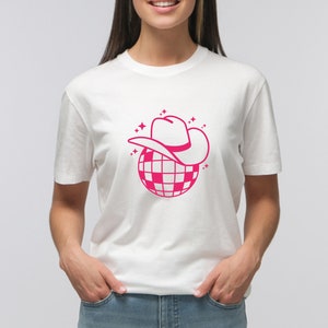 Pu&ograve; includere: Maglietta bianca con una grafica rosa di una palla da discoteca con un cappello da cowboy rosa in cima.