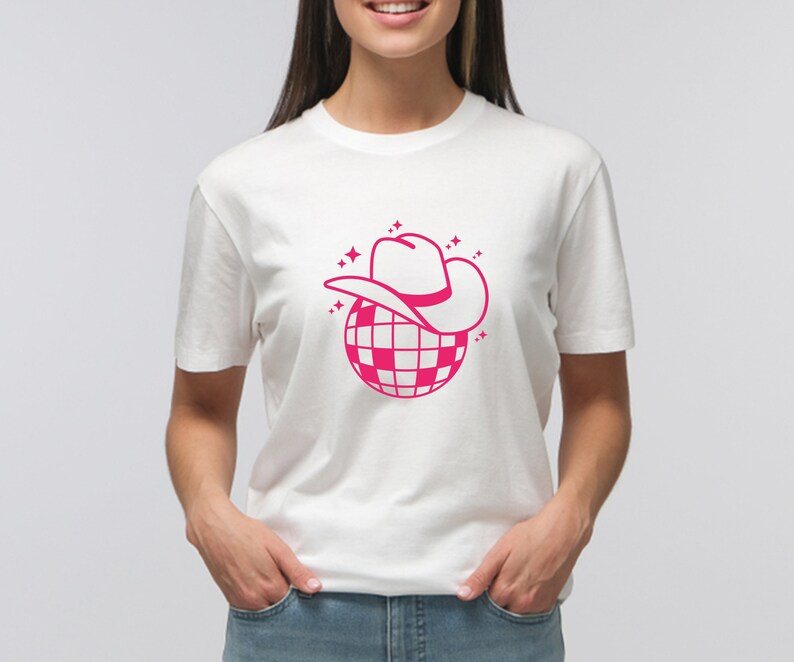 Pu&ograve; includere: Maglietta bianca con una grafica rosa di una palla da discoteca con un cappello da cowboy rosa in cima.