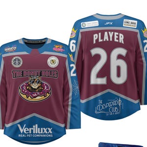 May include: A maroon and blue hockey jersey with the text "THE DONUT HOLES" and a cartoon cat wearing sunglasses inside a donut. The number "26" is on the back. The jersey also has the text "Veriluxx REAL PET COMPANIONS".