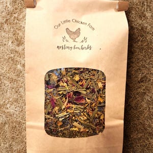 May include: A brown paper bag with a clear window showing a mix of dried herbs and flowers. The bag is labelled "Our Little Chicken Farm" with a chicken illustration and the words "nesting box herbs."