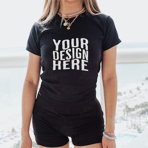 May include: A black t-shirt with the text "YOUR DESIGN HERE" printed in white. The shirt is being worn by a person standing on a balcony.