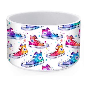 May include: White ceramic mug featuring a repeating pattern of colorful high-top sneakers. The sneakers are painted in watercolor style with rainbow gradients and a star logo on the ankle. Splashes of watercolor dots are scattered around the shoes.