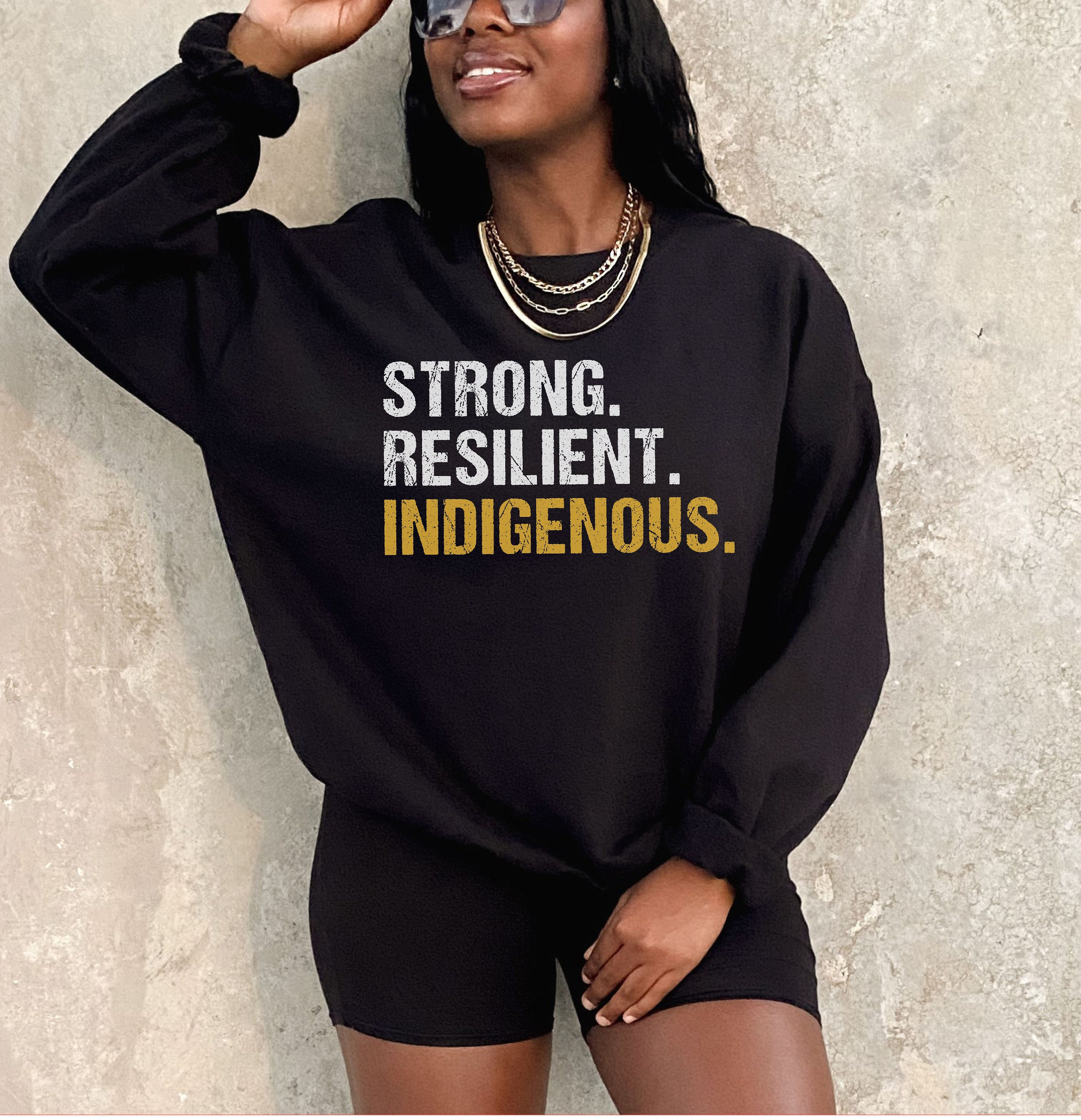 May include: Black sweatshirt with the text "STRONG. RESILIENT. INDIGENOUS." in white and gold lettering.