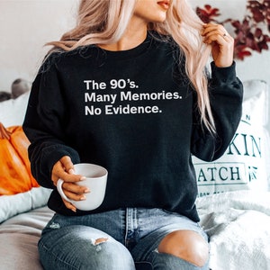 May include: A black sweatshirt with white text that reads "The 90's. Many Memories. No Evidence."