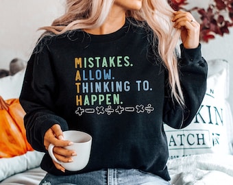 Op de afbeelding: Een zwart sweatshirt met een kleurrijke afbeelding met de tekst "Mistakes. Allow. Thinking To. Happen." met wiskundige symbolen onder de tekst.