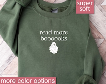 May include: Military green sweatshirt with the text "read more boooooks" and a white ghost graphic holding a book. The words "super soft" are in a pink box. The words "more color options" are in a pink box, and the words "military green" are written below.