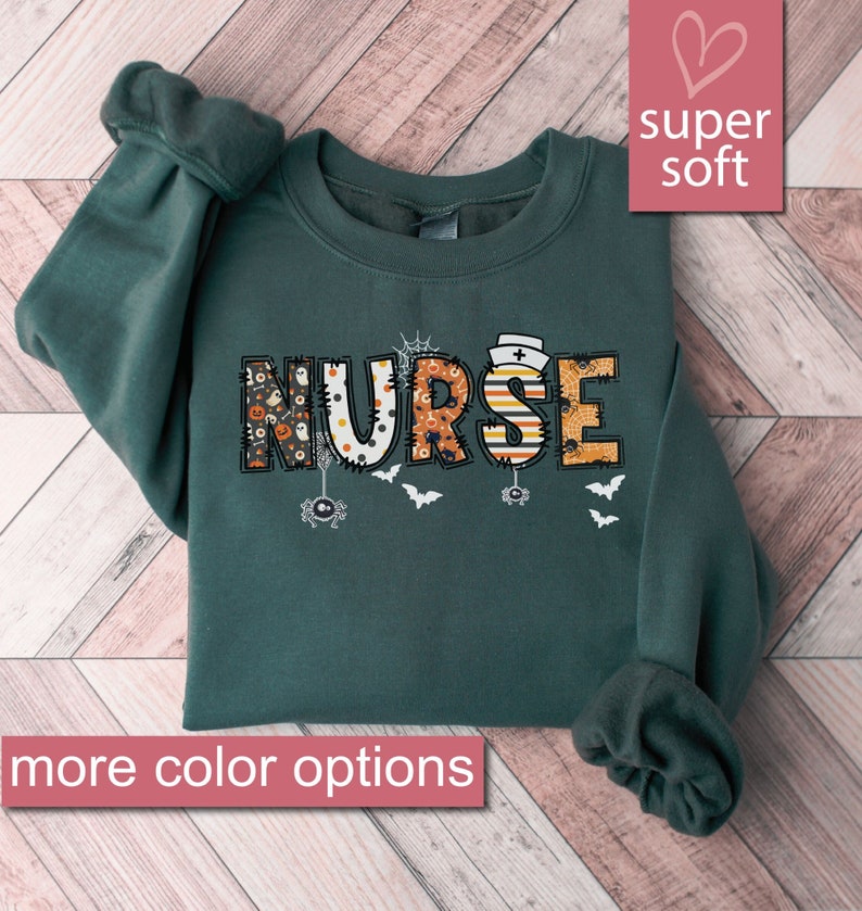 May include: A dark green sweatshirt with the word "NURSE" in colorful Halloween-themed letters. The letters are decorated with spiders, bats, and other Halloween imagery. The sweatshirt is super soft and has more color options.