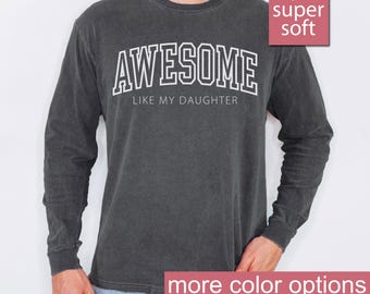 May include: A dark gray long-sleeve t-shirt with the text "AWESOME LIKE MY DAUGHTER" in white. The shirt is made of a soft, comfortable fabric.