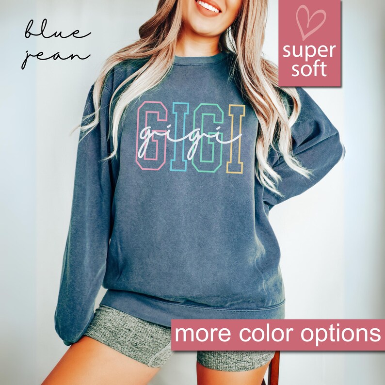 May include: A dark blue sweatshirt with the word "GIGI" in colorful letters and the text "gigi" in white script underneath. The sweatshirt is made of a soft, comfortable fabric and has a relaxed fit.