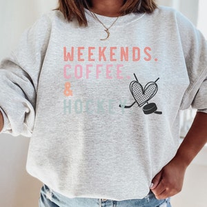 May include: Gray sweatshirt with the text "Weekends. Coffee & Hockey" in pink, orange, and blue. A heart with a hockey stick and puck is below the text.