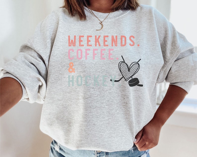 May include: Gray sweatshirt with the text "Weekends. Coffee & Hockey" in pink, orange, and blue. A heart with a hockey stick and puck is below the text.