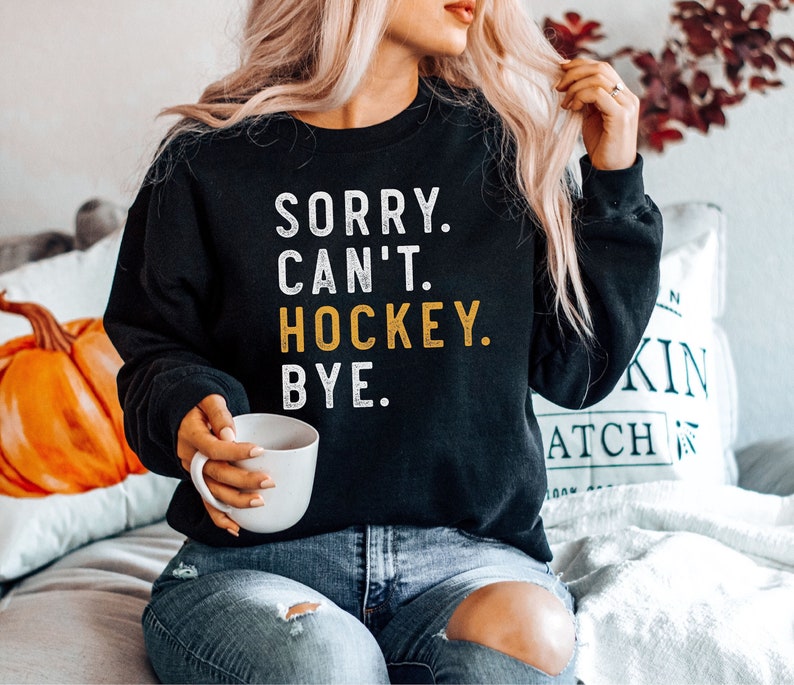 Op de afbeelding: Een zwart sweatshirt met de tekst "SORRY. CAN'T. HOCKEY. BYE." in witte en gele letters.