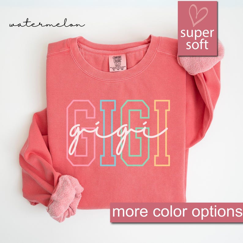 May include: A coral colored sweatshirt with the word "gigi" written in rainbow colors. The sweatshirt is made of a soft, comfortable fabric and has a crew neck.
