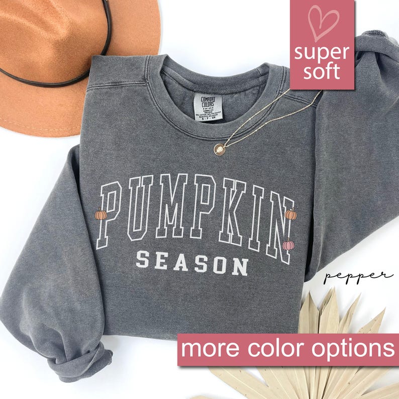 May include: A gray sweatshirt with the text "Pumpkin Season" in white with two small orange pumpkins on either side of the text. The sweatshirt is made of a soft, comfortable fabric.