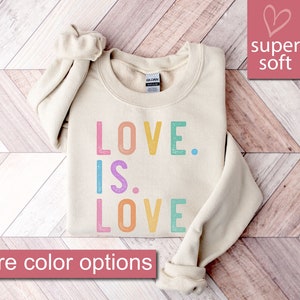 May include: A beige sweatshirt with the text "LOVE. IS. LOVE" in rainbow colors. The sweatshirt is made of super soft material.