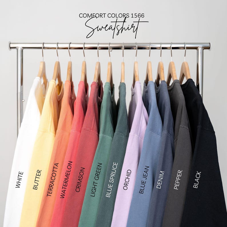 May include: A rack of 12 sweatshirts in various colors, including white, butter, terracotta, watermelon, crimson, light green, blue spruce, orchid, blue jean, denim, pepper, and black. The text "COMFORT COLORS 1566 Sweatshirt" is at the top of the image.