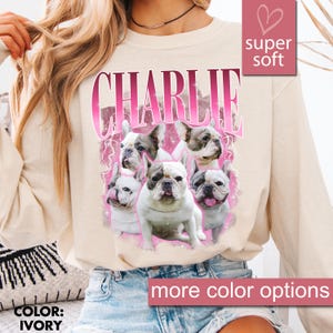 May include: Ivory-colored sweatshirt featuring the name "CHARLIE" in a pink, stylized font above a graphic of several French Bulldogs. The sweatshirt has a "super soft" label and a "more color options" label.