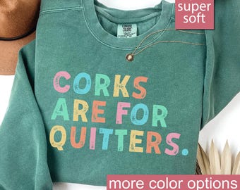 May include: A light green sweatshirt with the text "CORK ARE FOR QUITTERS." in rainbow colors. The sweatshirt is super soft and comfortable.