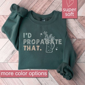 May include: A dark green sweatshirt with the text "I'd Propagate That." in white and beige lettering. A stylized illustration of a pitcher with flowers is to the right of the text.