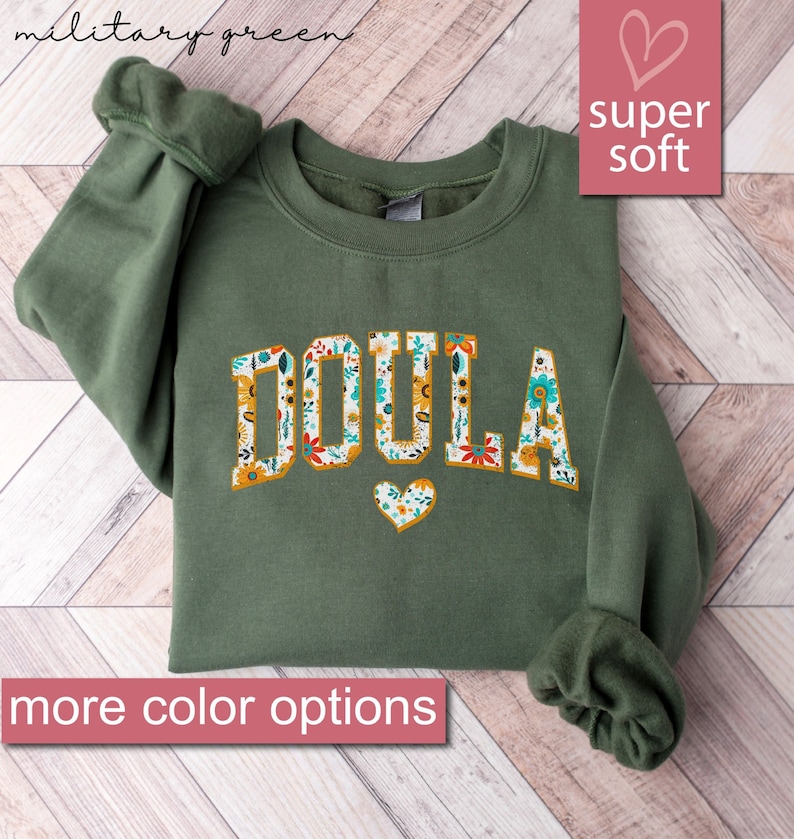 May include: A green sweatshirt with the word "DOULA" printed in white letters with a floral pattern. The sweatshirt is super soft and has a heart design below the word.
