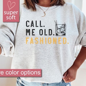 May include: A gray sweatshirt with the text "CALL. ME OLD. FASHIONED." in black and yellow. A black and white illustration of an old fashioned cocktail glass with ice and a cherry is next to the text.