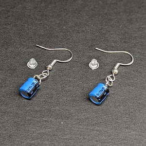 Puede incluir: Un par de pendientes de plata con abalorios cilíndricos azules. Los abalorios tienen texto negro que dice "100uF 25V".