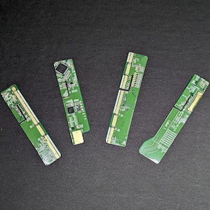 May include: Four green circuit boards with gold and white detailing are arranged on a black surface. The boards have various electronic components and traces visible. The boards are rectangular with a slightly curved shape.