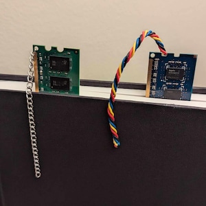May include: Two computer memory chips, one green and one blue, are used as bookmarks in a black notebook. A silver chain hangs from the green chip.