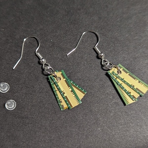 Op de afbeelding: Een paar oorbellen gemaakt van gerecyclede computergeheugenchips. De oorbellen zijn groen en goud en hebben zilveren haakjes.