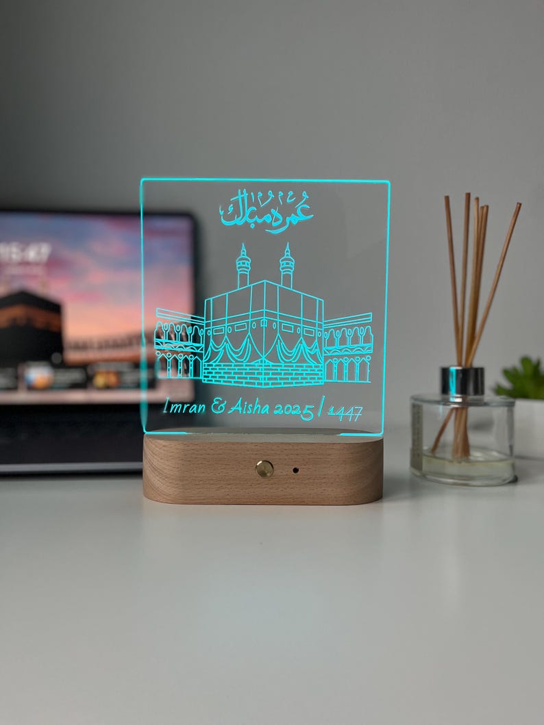 May include: A rectangular, illuminated LED night light with a wooden base. The light features a blue outline of a building and Arabic script. The text "Imran & Aisha 2025/1447" is also visible.