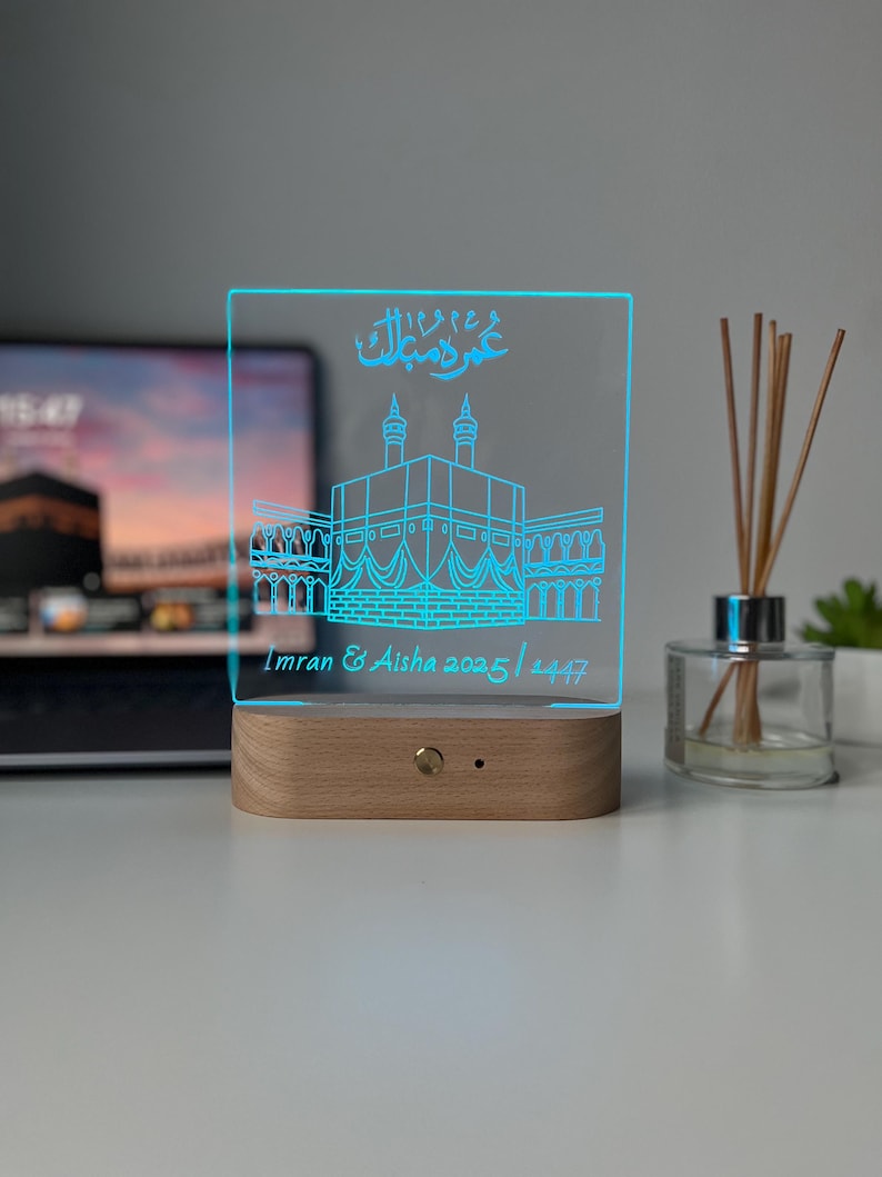 May include: A rectangular LED night light with a wooden base. The clear acrylic panel features a blue outline of a building with Arabic script above it. The names "Imran & Aisha" and the dates "2025 / 1447" are also displayed.