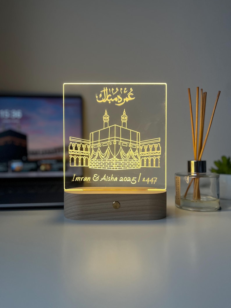 May include: A glowing LED night light with a rectangular acrylic panel featuring an etched illustration of a religious building. The base is made of wood. The text "Imran & Aisha 2025/1447" is visible.
