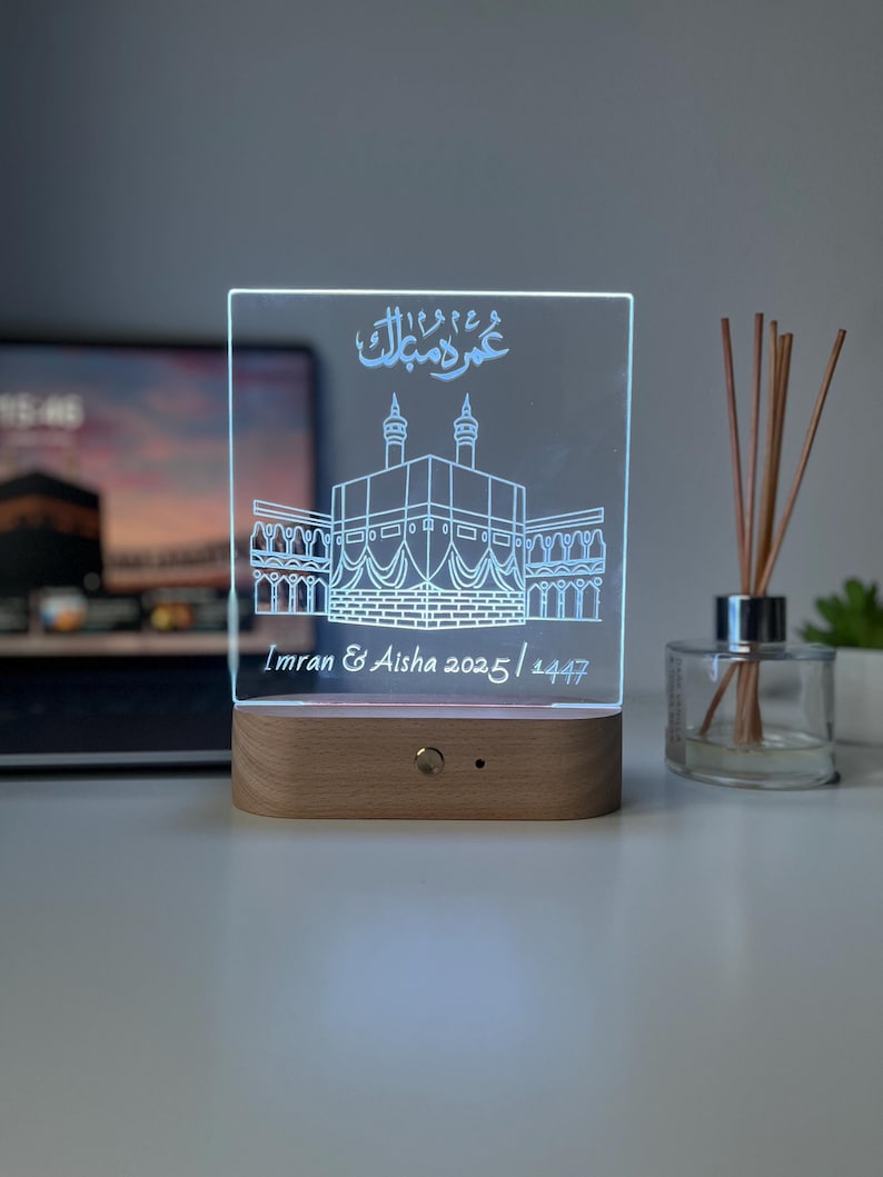 May include: A rectangular LED night light with a wooden base. The clear acrylic panel features an etched illustration of a religious building and Arabic script. The names "Imran & Aisha 2025 / 1447" are also etched on the panel.