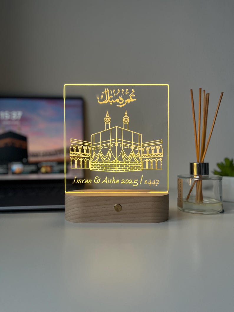 May include: A rectangular LED lamp with a wooden base. The clear acrylic panel features an etched illustration of a religious structure and Arabic script. The text "Imran & Aisha 2025/1447" is also etched on the panel.
