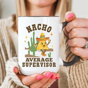 May include: White ceramic mug with a black handle. The mug has a cartoon image of a nacho chip wearing a sombrero and the text "Nacho Average Supervisor".