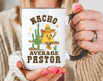 May include: White ceramic mug with a black handle. The mug features a cartoon illustration of a nacho wearing a sombrero and the text "Nacho Average Pastor".