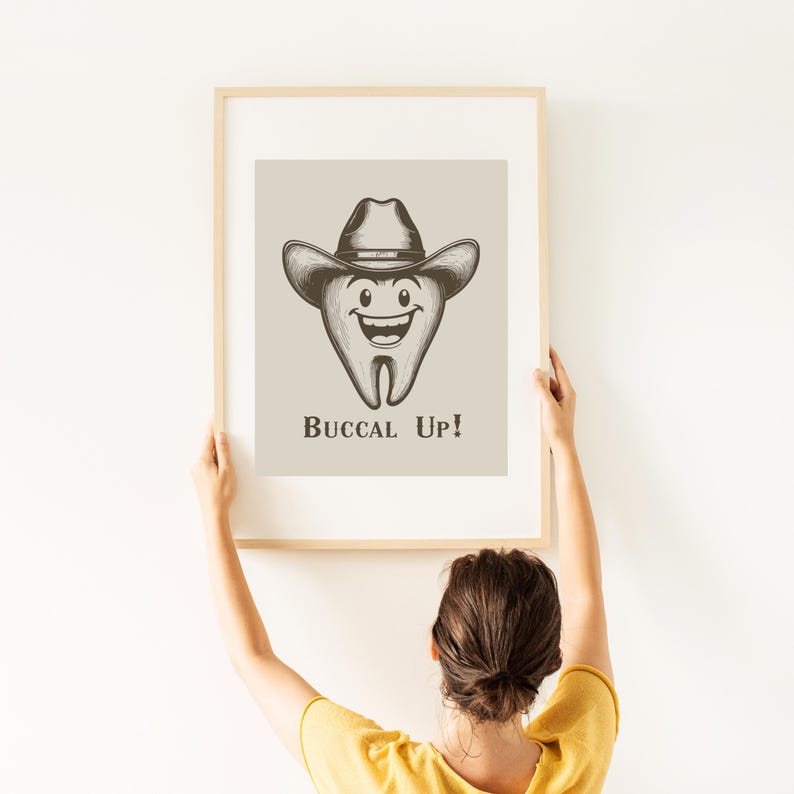 May include: A framed print with a cartoon illustration of a smiling tooth wearing a cowboy hat. The text "Buccal Up!" is below the tooth.