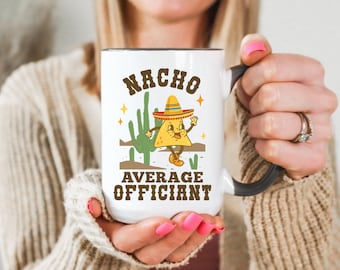 May include: White ceramic mug with a black handle and rim, featuring a cartoon nacho character wearing a sombrero. The mug has the text "NACHO AVERAGE OFFICIANT" in brown lettering, with a cactus graphic.