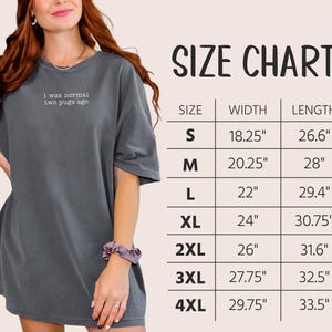 May include: A grey oversized t-shirt with the embroidered text "i was normal two pugs ago." A size chart is displayed, showing measurements in inches for width and length, ranging from size S to 4XL. The width measurements are between 46.35 cm and 75.57 cm.