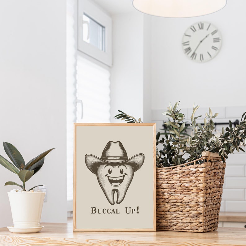 May include: A beige framed print with a cartoon tooth wearing a cowboy hat and the text "Buccal Up!" The tooth is smiling and has a happy expression.