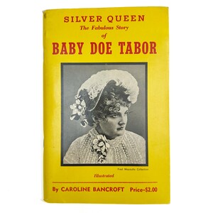 Puede incluir: Un libro antiguo con una cubierta amarilla, titulado "SILVER QUEEN The Fabulous Story of BABY DOE TABOR". La portada presenta un retrato en blanco y negro de una mujer con un sombrero con plumas. El libro está ilustrado por Caroline Bancroft.