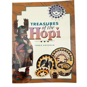 Puede incluir: Una portada de libro titulada "Treasures of the Hopi" con una figura nativa americana y cestas tejidas. La portada tiene un borde marrón y un emblema plateado en forma de sol. El nombre del autor, Theda Bassman, también es visible.