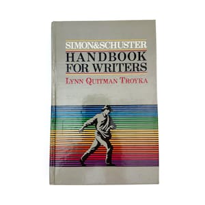 May include: A hardback book titled "Simon & Schuster Handbook for Writers" by Lynn Quitman Troyka. The cover shows a silhouette of a person walking, set against a rainbow-striped background.