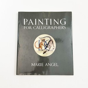 May include: A book titled "PAINTING FOR CALLIGRAPHERS" by Marie Angel. The cover is dark gray with white text. A circular illustration in the center features two lemurs and the letters "DC".