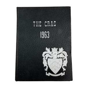 May include: A black yearbook titled "THE CRAG 1963" with a silver emblem on the lower right corner. The cover has a textured appearance. The emblem features a crest with a crown and scroll.