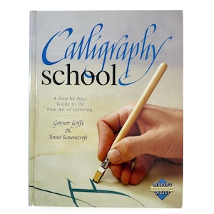 May include: A book titled "Calligraphy School" with blue and black text. The cover shows a hand holding a calligraphy pen. The book is a step-by-step guide to the fine art of lettering, by Gaynor Goffe & Anna Ravenscroft.
