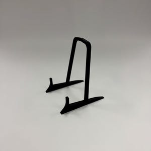 May include: A black metal display stand with a curved top and two supporting legs. The stand is designed to hold and showcase items. The stand is on a white background.