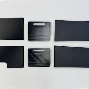 May include: A collection of black rectangular components including two flat panels with side cutouts, two smaller panels with top handle slots, and two larger elongated panels with rounded edges and side notches, all arranged on a plain surface.