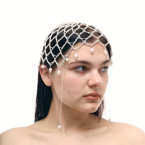 May include: A delicate, white crocheted headpiece with a net-like design. Small, dangling pearls are attached to the headpiece and hang down. The headpiece is worn on the head.